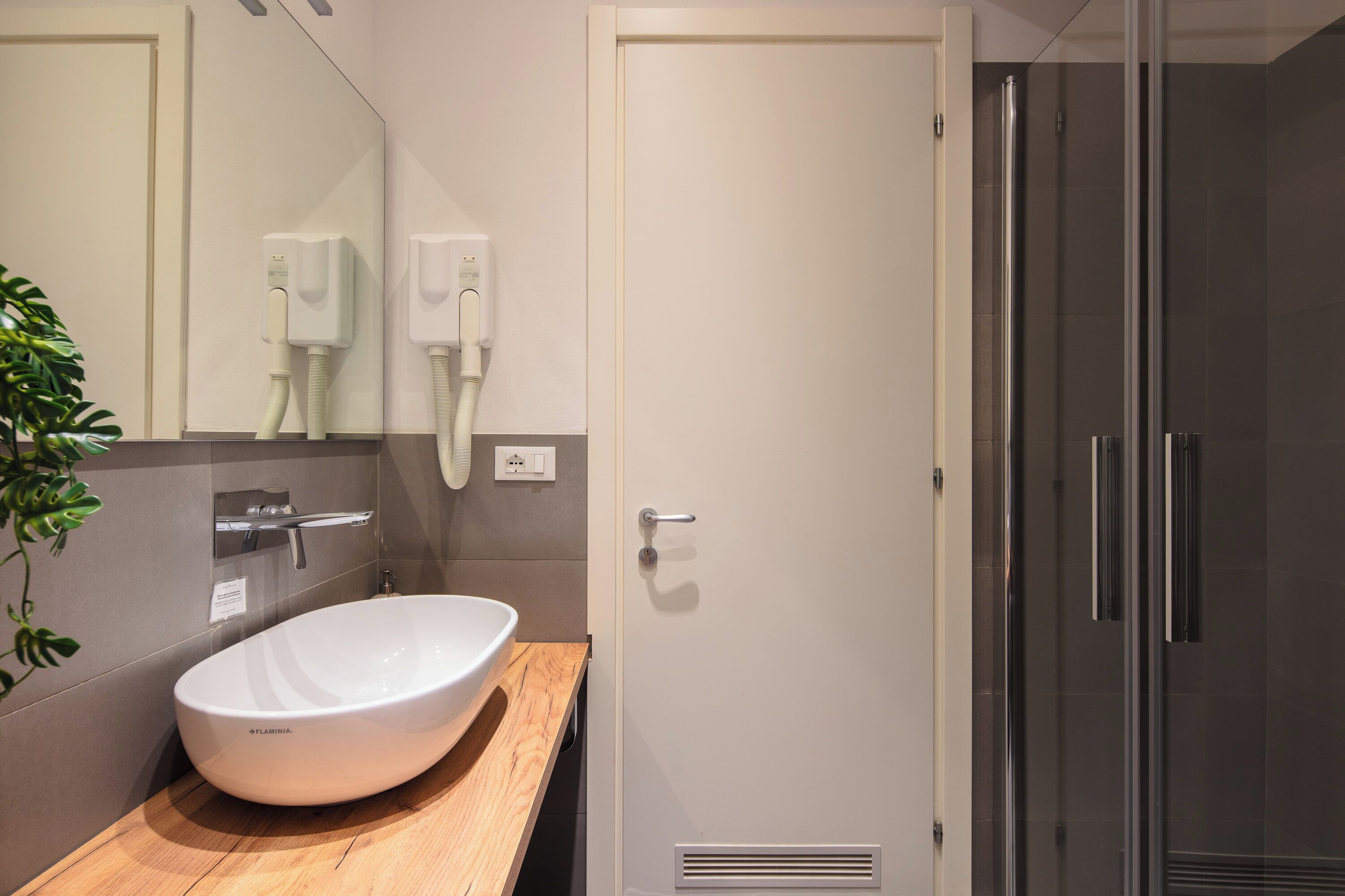 Un baño moderno con lavamanos blanco, espejo, secador de pelo y cabina de ducha.