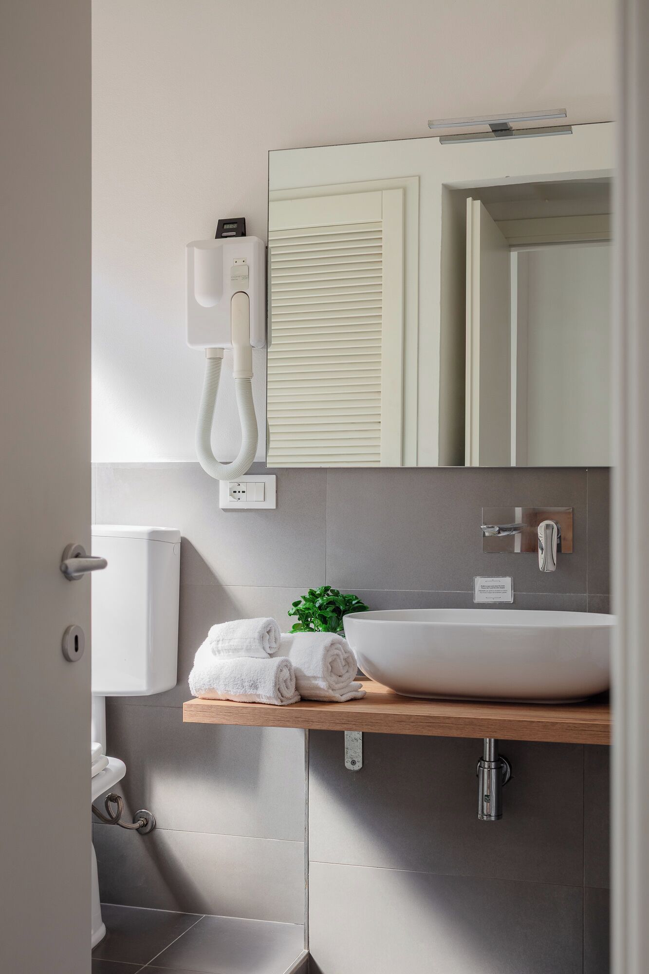 Un bagno moderno con lavandino bianco, porta asciugamani, specchio e termosifone a parete.