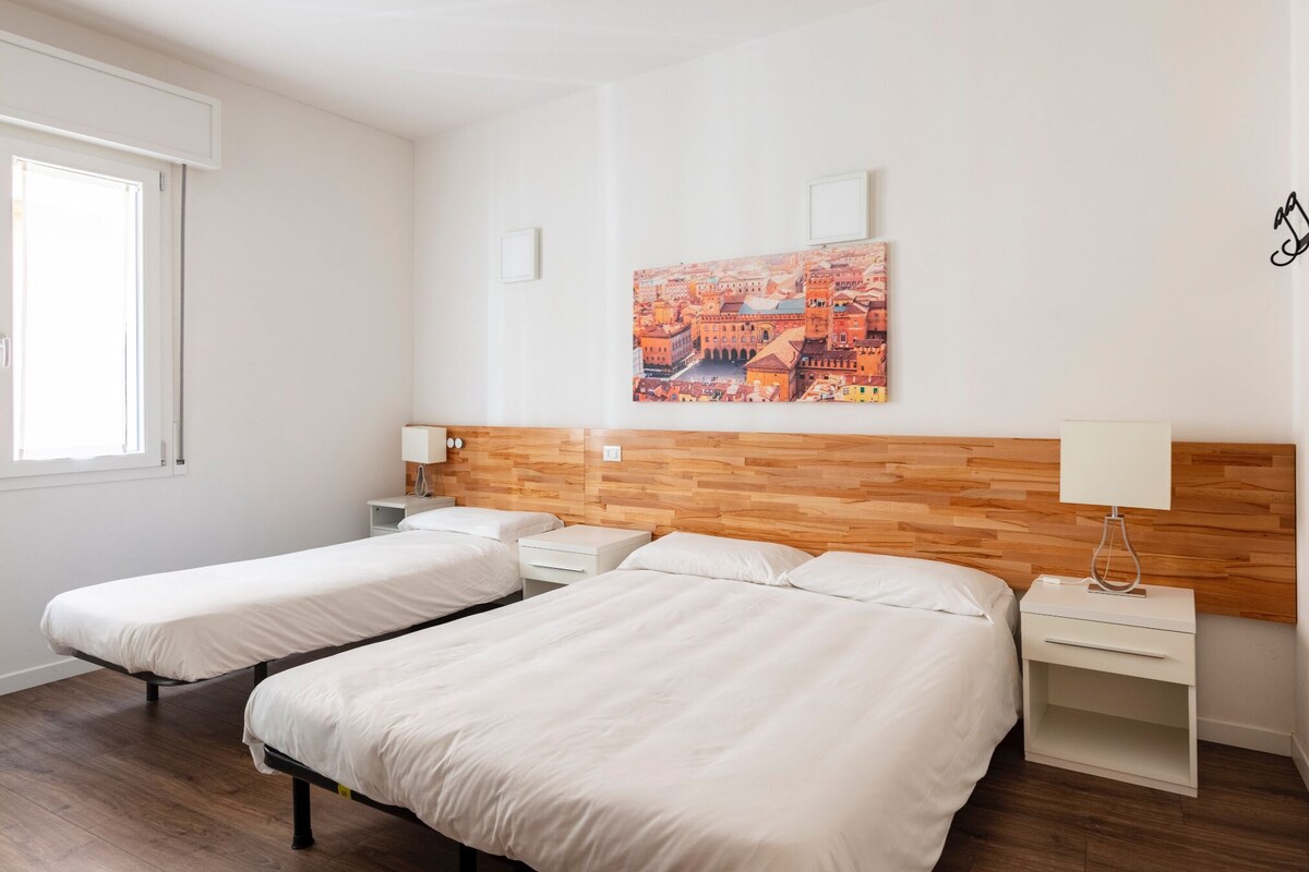 Ein Hotelzimmer mit zwei Betten, einem Holzkopfende, einem Stadtbild, einem Fenster und einer Wandleuchte.