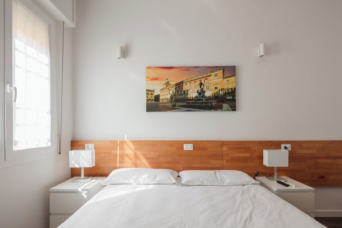 Ein Hotelzimmer mit einem Bett, zwei Nachttischen, einem Wandbild und einem Fenster.