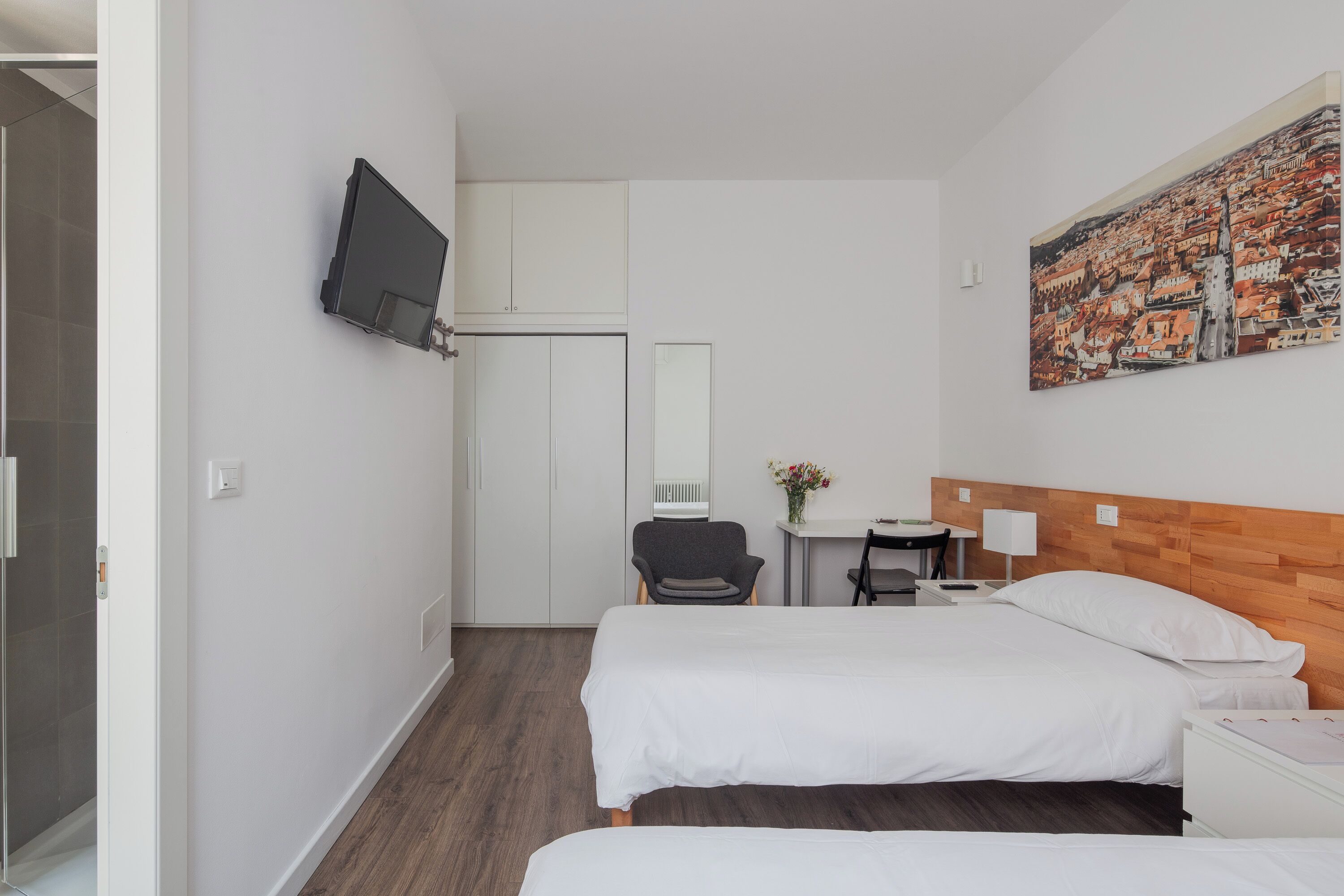 A hotel room with two beds, a TV, a desk with a chair, a painting, and a wooden headboard.