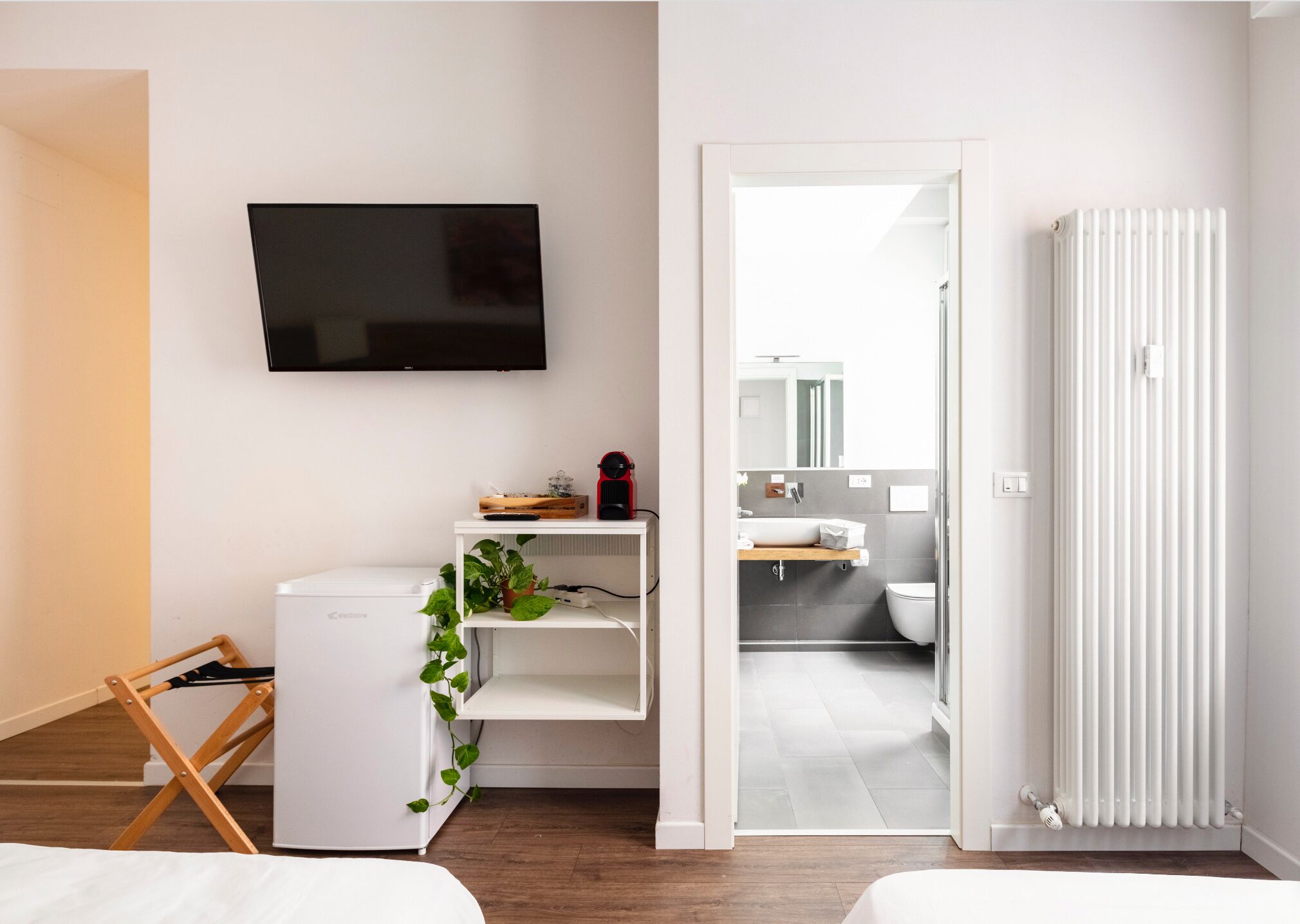 Un dormitorio moderno con cama, televisor, radiador y vistas al baño.