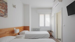 A hotel room with two beds, a wooden headboard, a radiator, a window, a TV, and a painting on the wall. - Strazzacappe Comfort Rooms by Wonderful Italy (Bologna)