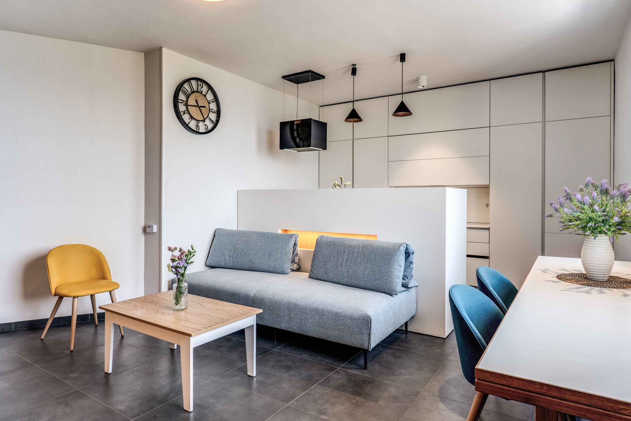A modern living room with a sofa, a wooden table, a yellow chair, and a dining table with chairs.