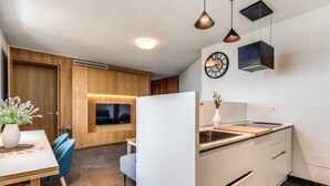 A modern kitchen with white cabinets, a wooden dining table, blue chairs, and pendant lighting. - Suite Priora with sea view (Priora)