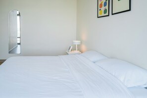 A hotel room with a bed, a nightstand with a lamp, and a wall-mounted mirror. - Nordic Minimal 3BR Tub • Near Impact Arena • DMK (Chang Wat Nonthaburi)