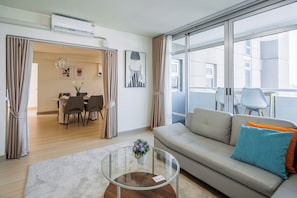 A modern living room with a sofa, a glass coffee table, and a dining area with chairs and a table.