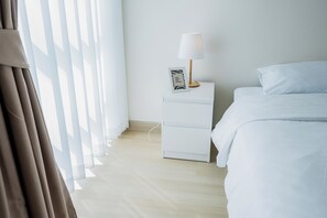 Quarto de hotel com cama, mesa de cabeceira com abajur e janela com cortinas.