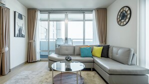 A modern living room with a sectional sofa, a round coffee table, and a large window with curtains.