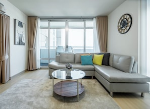 A modern living room with a sectional sofa, a round coffee table, and a large window with curtains.