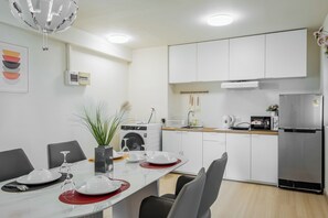 A modern kitchen with white cabinets, stainless steel appliances, and a dining area with a table set for four. - Nordic Minimal 3BR Tub • Near Impact Arena • DMK (Chang Wat Nonthaburi)