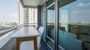 A balcony with a table and chairs, a glass partition, and a city view.