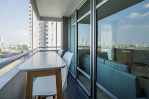 A balcony with a table and chairs, a glass partition, and a city view.
