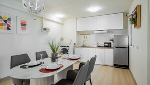 A modern kitchen with white cabinets, a stainless steel refrigerator, and a dining area with a round table set for four.