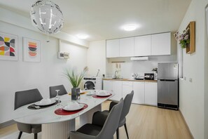 A modern kitchen with white cabinets, a stainless steel refrigerator, and a dining area with a round table set for four.
