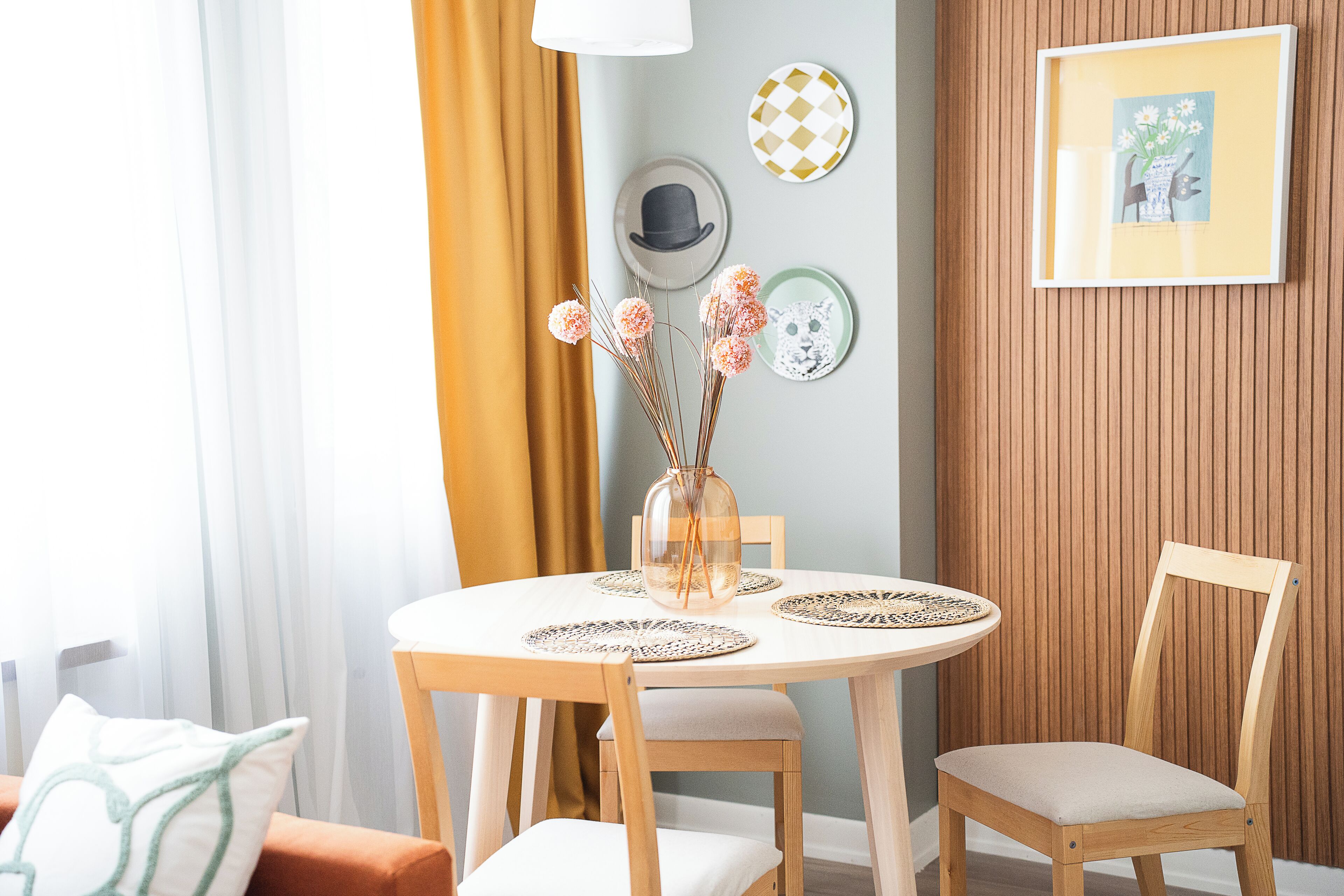 Ein Essbereich mit rundem Tisch, Stühlen, einer Vase mit Blumen und Wanddekorationen.
