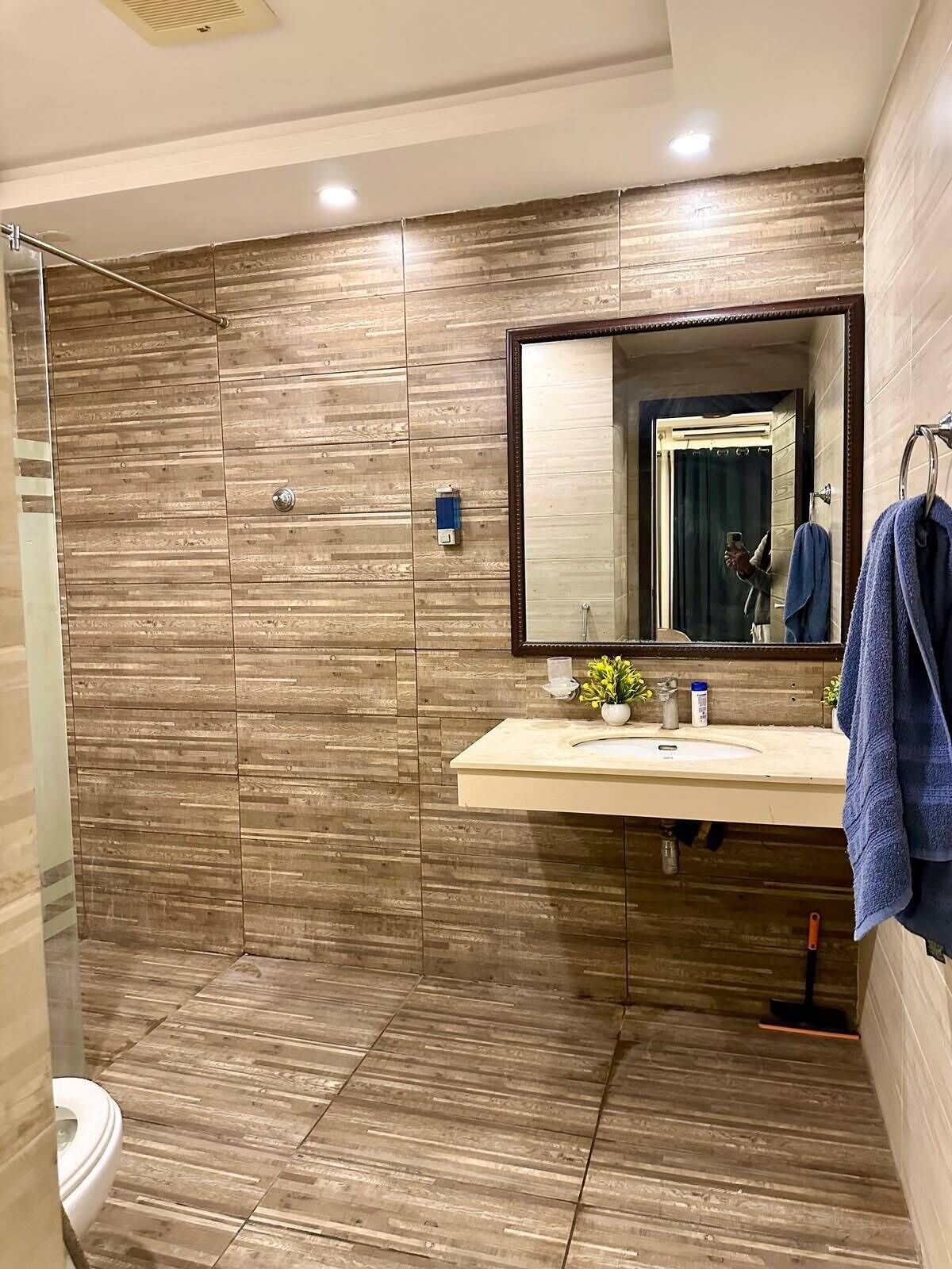 Un baño moderno con pared de madera, un espejo grande, un lavamanos y una zona de ducha.
