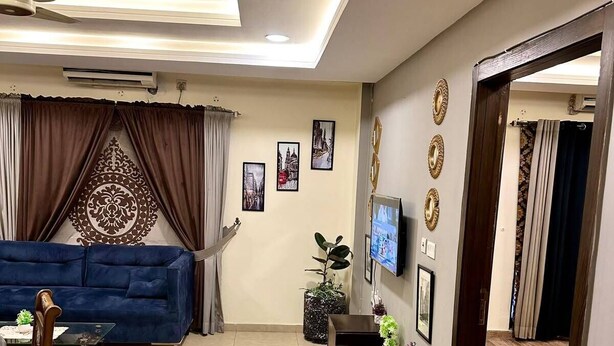 Ein Wohnzimmer mit einer Couch, Couchtisch, Fernseher, Wanddekoration, Deckenventilator und einer Zimmerpflanze.