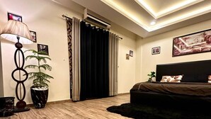 Ein Schlafzimmer mit Bett, Deckenventilator, Topfpflanze, Lampe und großem Fenster mit Vorhängen.