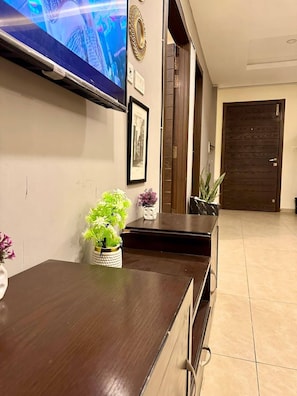 A living room with a flat-screen TV mounted on the wall, a dark wooden coffee table, a framed picture, and a door in the background.