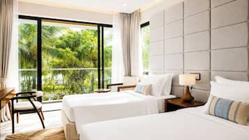 A hotel room with two beds, a desk, and a chair. There is a large window with a view of greenery outside.