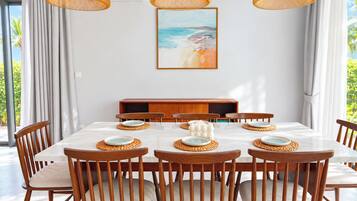 Un comedor con una mesa blanca, sillas de madera, individuales tejidos y un cuadro con temática marina en la pared.