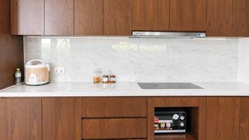 A kitchen with wooden cabinets, a marble countertop, a rice cooker, a water bottle, and a built-in microwave.