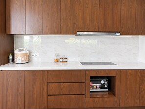 Una cocina con armarios de madera, encimera de mármol, una olla arrocera, una botella de agua y un microondas integrado.