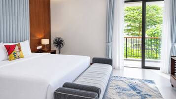 Habitación de hotel moderna con una cama grande, un banco, un ventilador y vistas a zonas verdes a través del balcón.