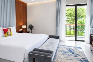 Habitación de hotel moderna con una cama grande, un banco, un ventilador y vistas a zonas verdes a través del balcón.