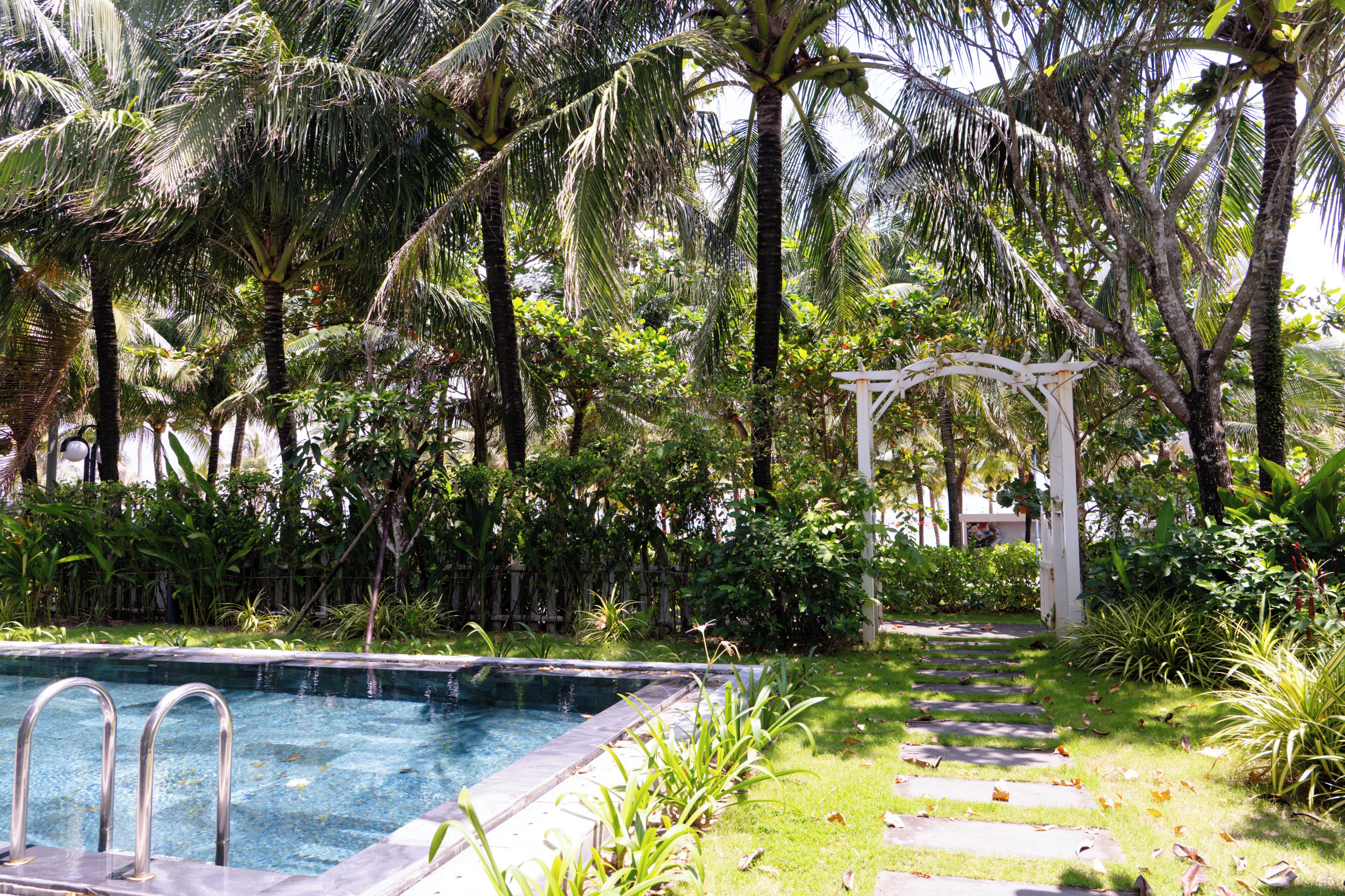 A swimming pool surrounded by lush greenery and a white pergola.