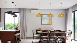 A modern dining area with a wooden table and chairs, pendant lighting, and a large window with a view.
