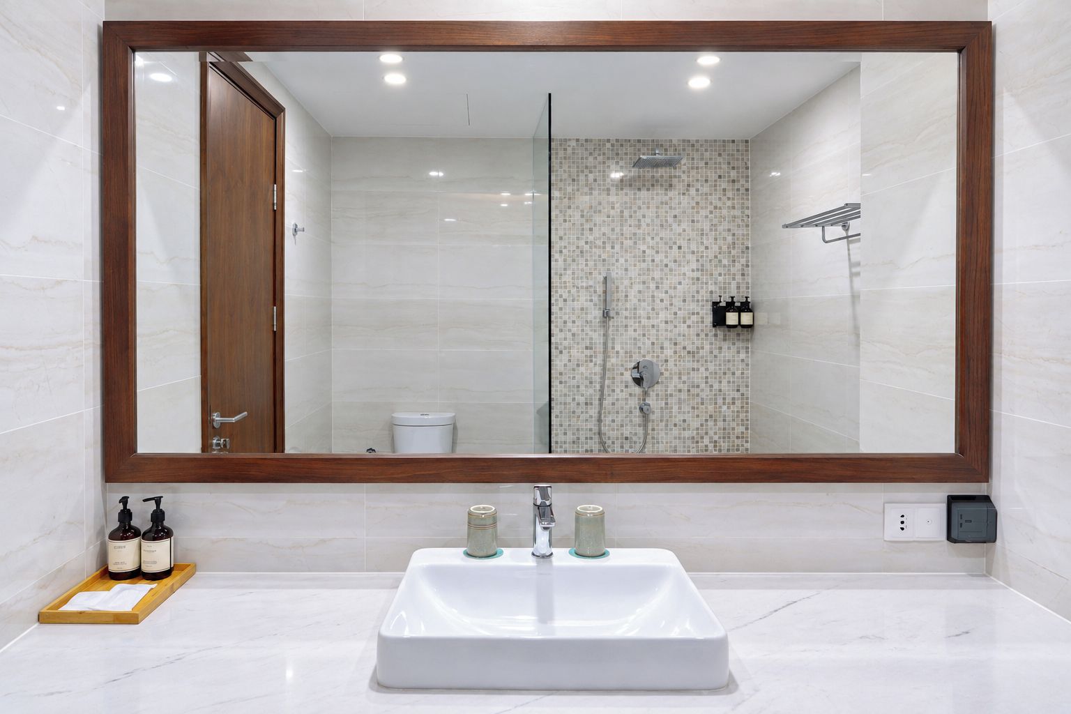 Un baño con un espejo grande, un lavamanos blanco y una zona de ducha.