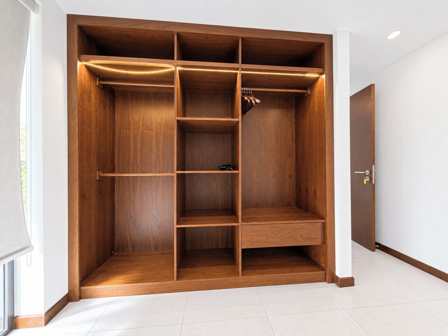 Un vestidor amplio con varias estanterías y espacio para colgar, una puerta con cerradura y suelo de baldosas.