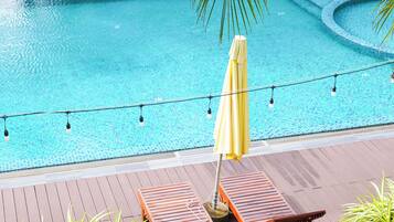 A swimming pool with lounge chairs and umbrellas, surrounded by palm trees and plants.
