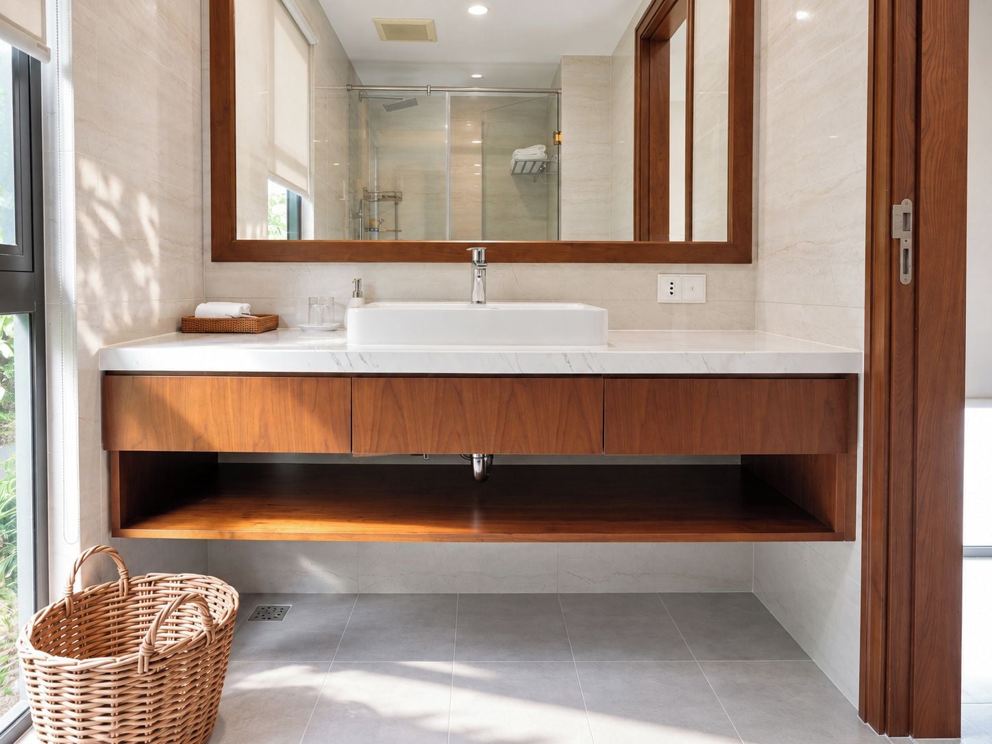 A modern bathroom with a large mirror, white sink, wooden vanity, and a wicker basket.