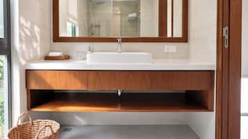A modern bathroom with a large mirror, white sink, wooden vanity, and a wicker basket.