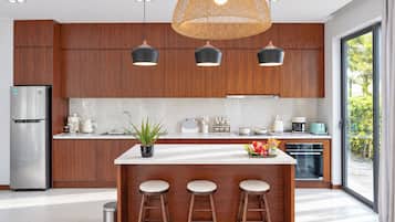 A modern kitchen with wooden cabinets, a stainless steel refrigerator, a central island with stools, and pendant lighting.