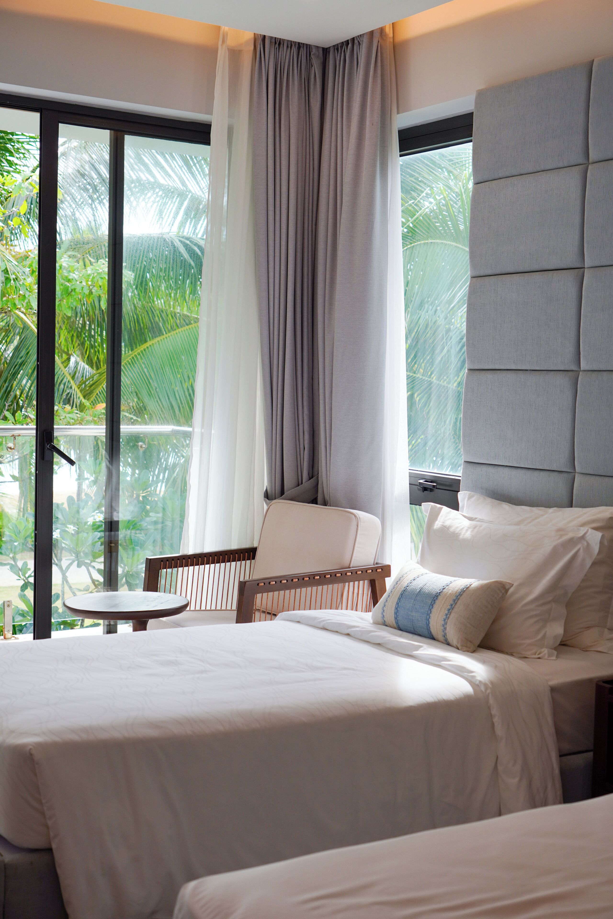 Habitación de hotel con cama, una silla, un ventanal con cortinas y vistas a zonas verdes.