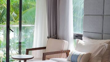 Habitación de hotel con cama, una silla, un ventanal con cortinas y vistas a zonas verdes.