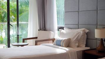 A hotel room with a bed, a chair, a nightstand, a lamp, and a view of greenery through the window.