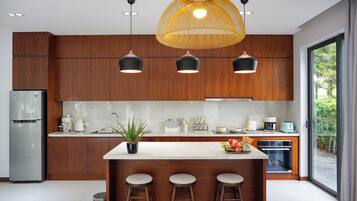 A modern kitchen with a central island, bar stools, a refrigerator, and a large window with a view of greenery.