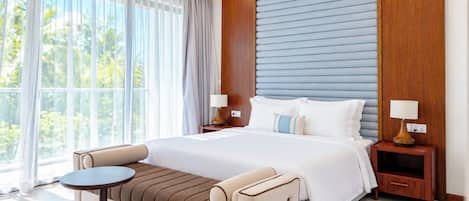 A modern hotel room with a large bed, a sofa bed, a small round table, and a nightstand with lamps.
