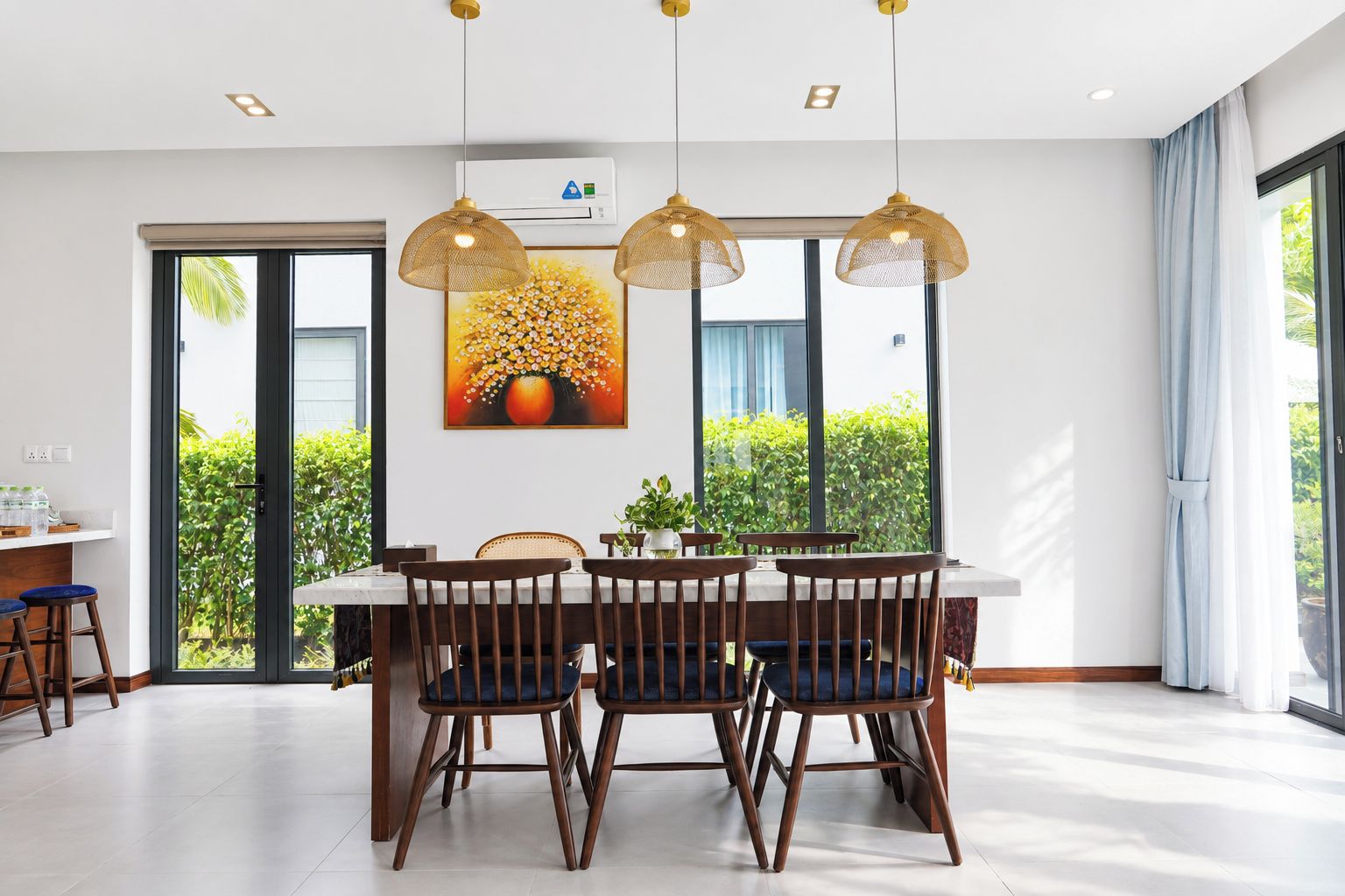 Un comedor moderno con una mesa, sillas, luces colgantes y un ventanal con vistas a zonas verdes.