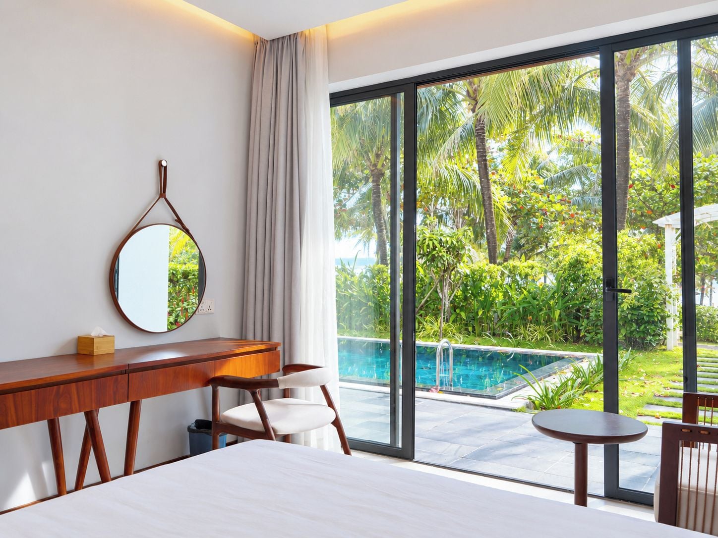 A hotel room with a large window, a bed, a desk, a chair, and a small table.