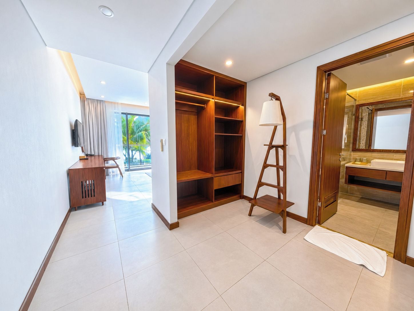A hotel room with a wooden wardrobe, a desk, a lamp, and a bathroom visible through an open door.
