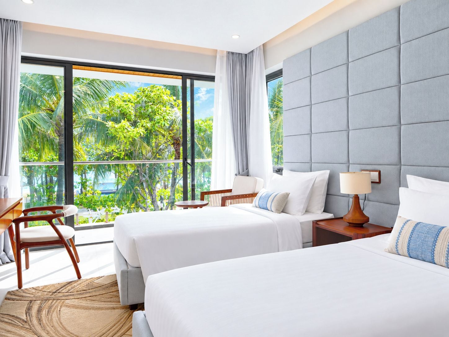 Habitación de hotel con dos camas, un escritorio y vistas a un follaje exuberante.