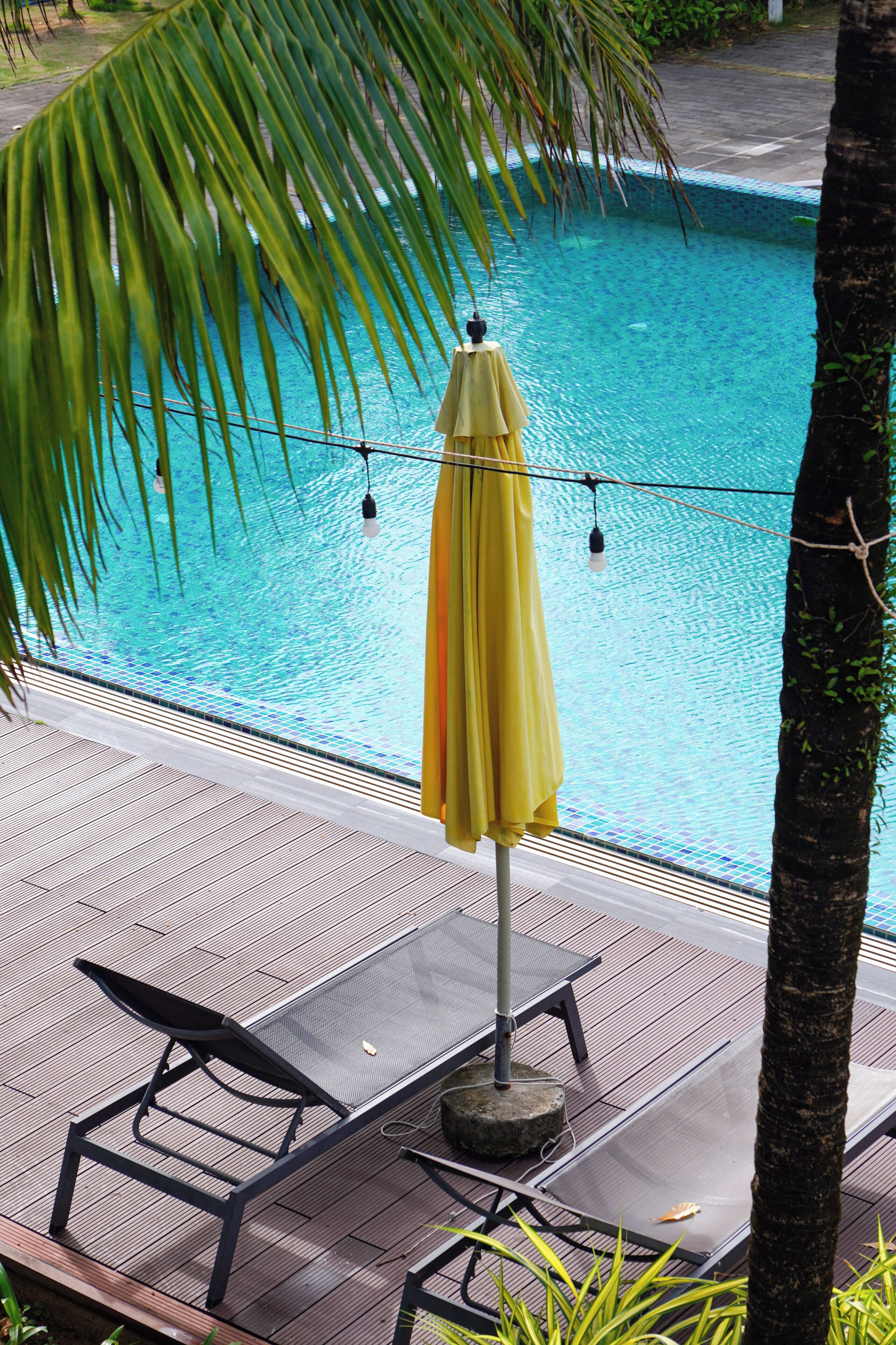 A poolside area with a yellow umbrella, lounge chairs, and a tiled pool.