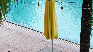 A poolside area with a yellow umbrella, lounge chairs, and a tiled pool.