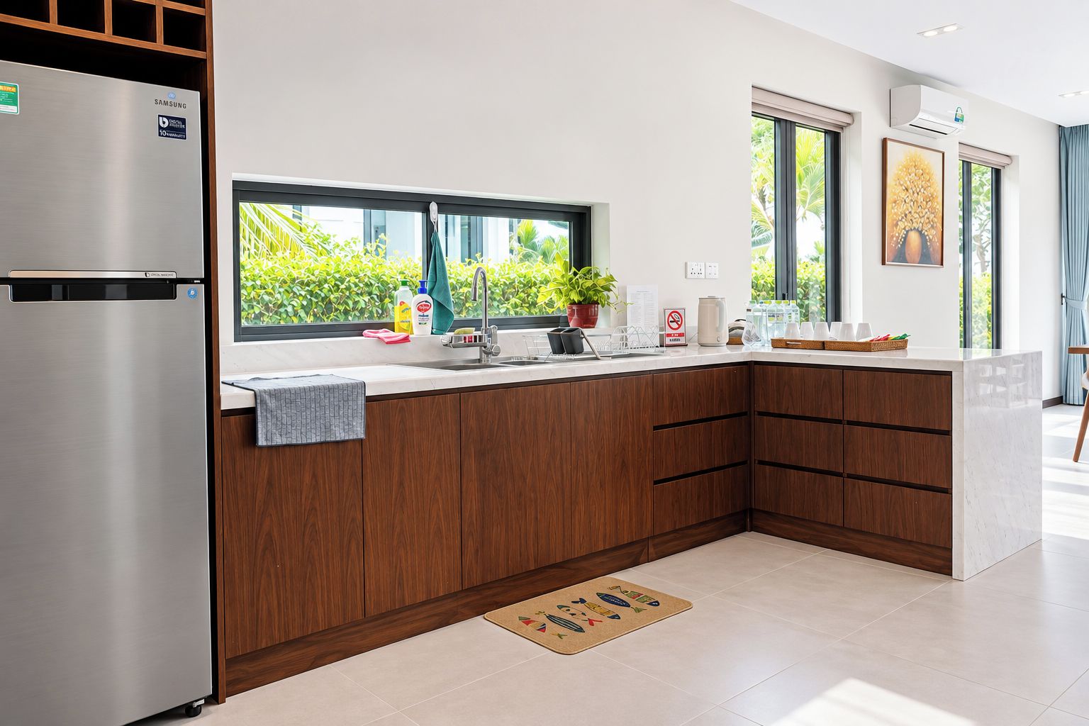 A modern kitchen with a stainless steel refrigerator, wooden cabinets, a window with a view of greenery, and a countertop with various items.